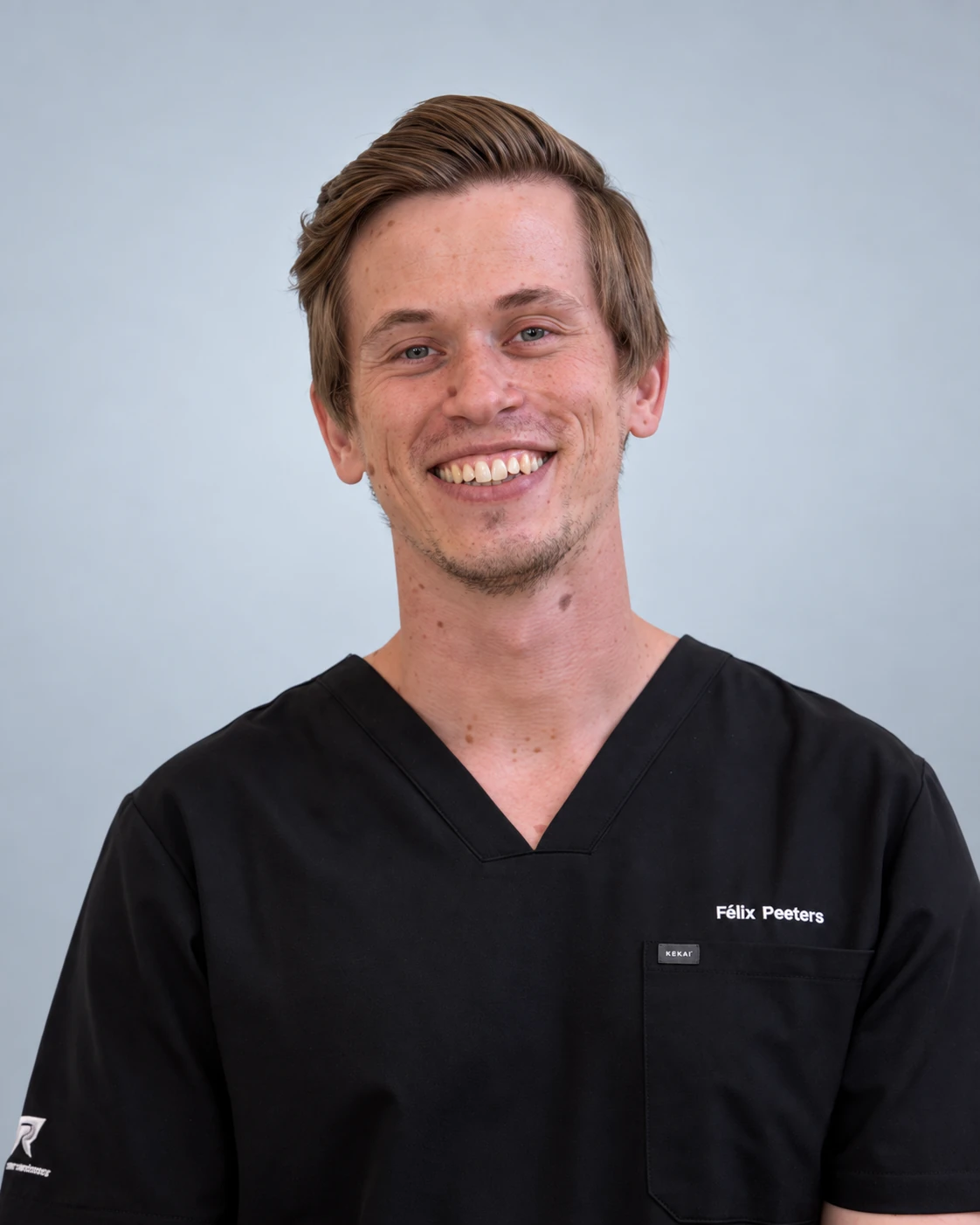 Felix Peeters wearing black scrubs against a light neutral background.
