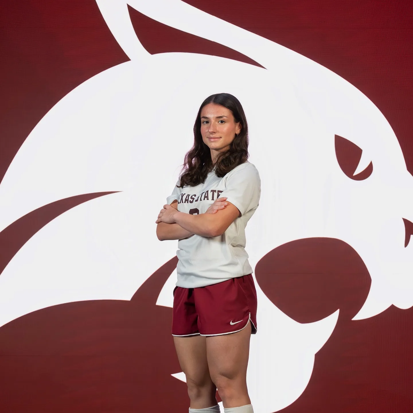 Ginny wearing her Texas State football kit in front of the university’s bobcat emblem.
