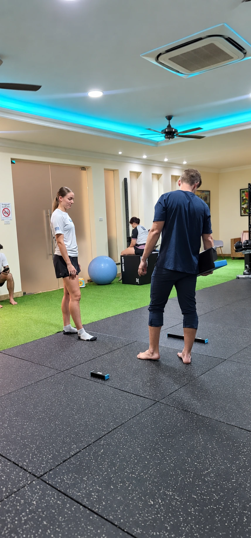 An athlete and coach preparing for a jump assessment with sensors on the gym floor.