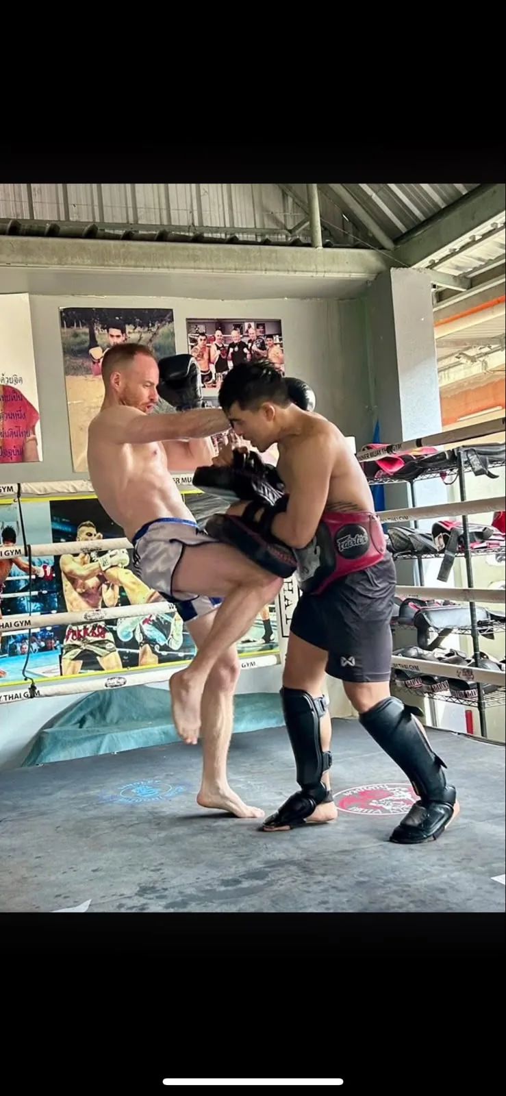 Kevin practising a knee strike with a pad holder in a Muay Thai ring.