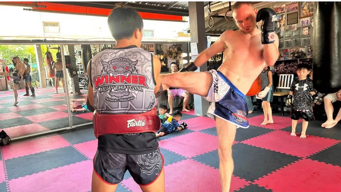 Kevin practising a kick with a pad holder at Muay Thai training.
