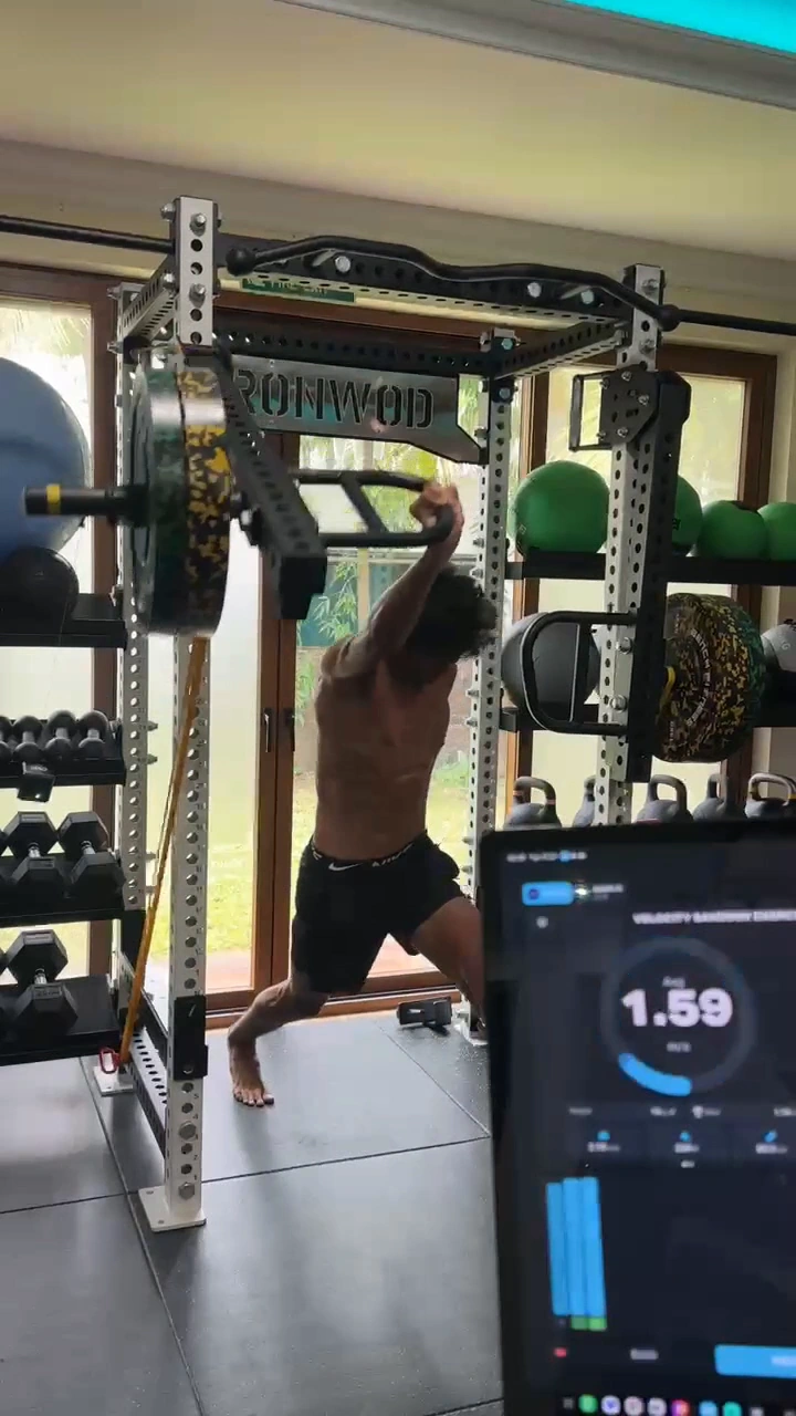 An athlete performing a landmine press with training feedback displayed nearby.